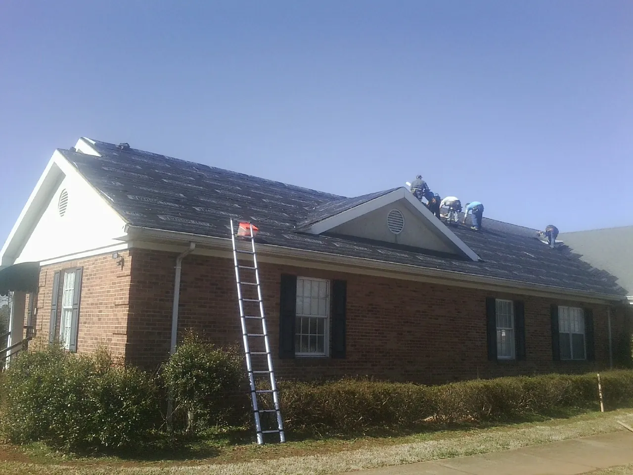 Crew tearing shingles off a brick ranch roof with a ladder set — Metal Roof Repair work by our crew in West Jefferson