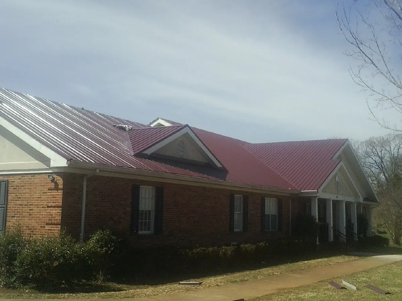 Red metal roof with gabled entries on a long brick building, from a Hail Damage Roof Repair job in West Jefferson