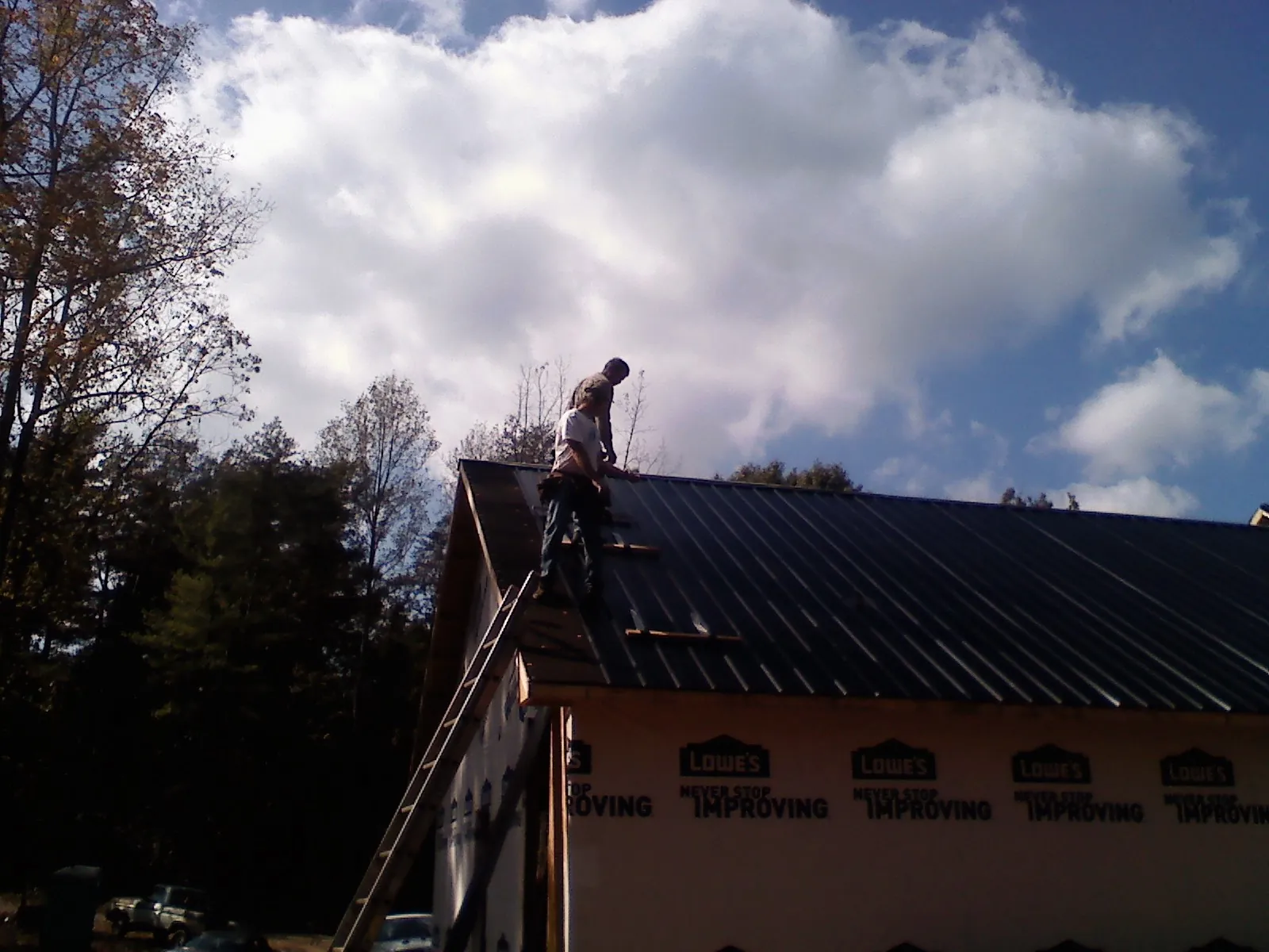 Roofer fastening dark metal panels high against a cloudy sky, from a Roof Inspection job in West Jefferson