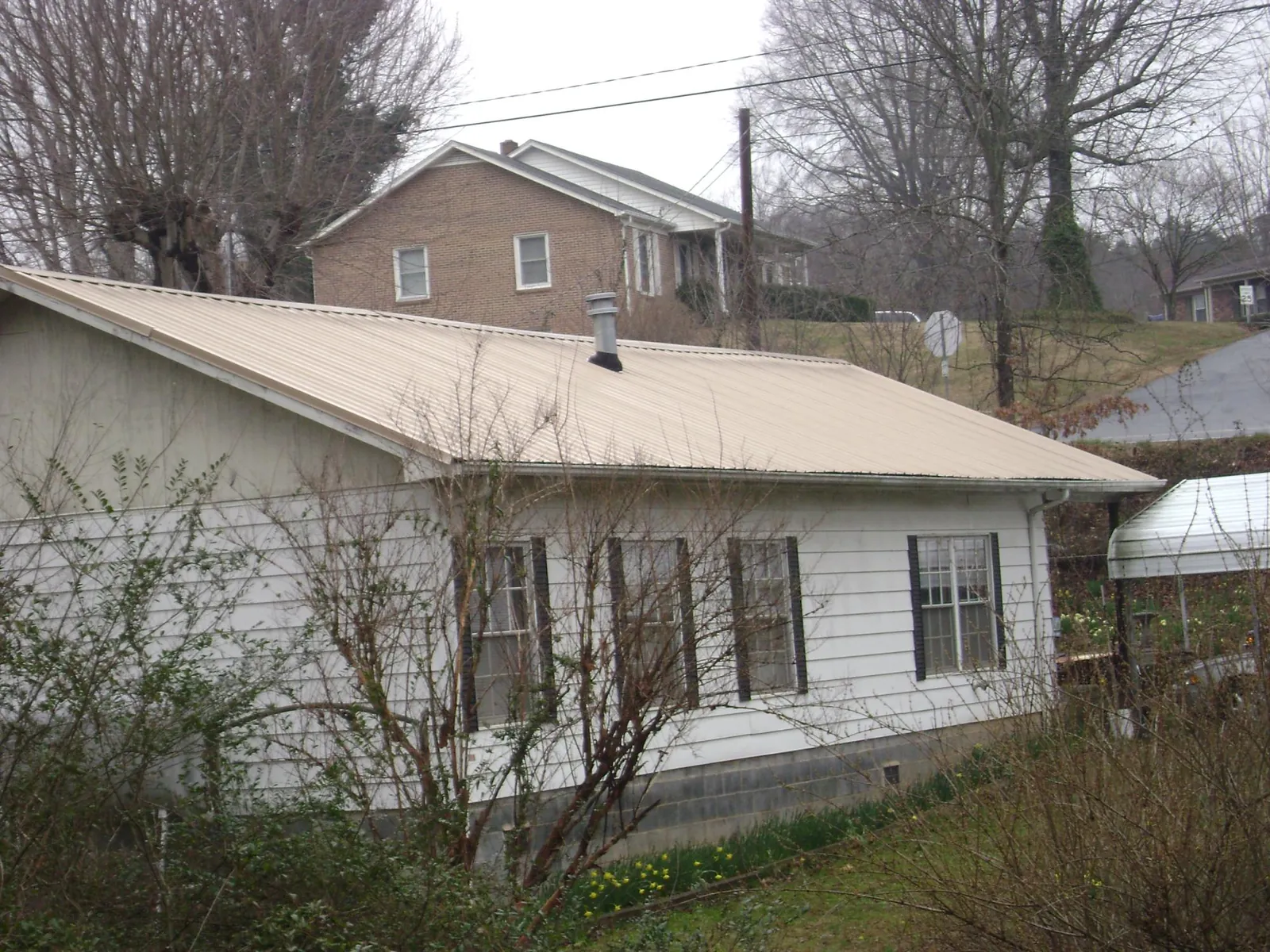 Tan metal roof on a white sided house set into a hillside — Commercial Roofing by Roofing Brothers in West Jefferson